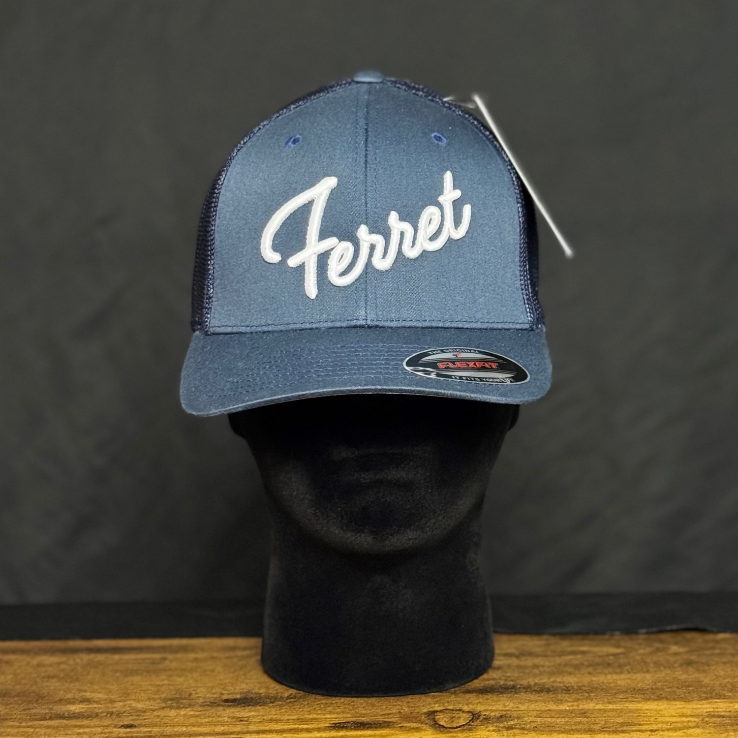 Blue cap with 'Ferret' logo on a black mannequin head against a dark background