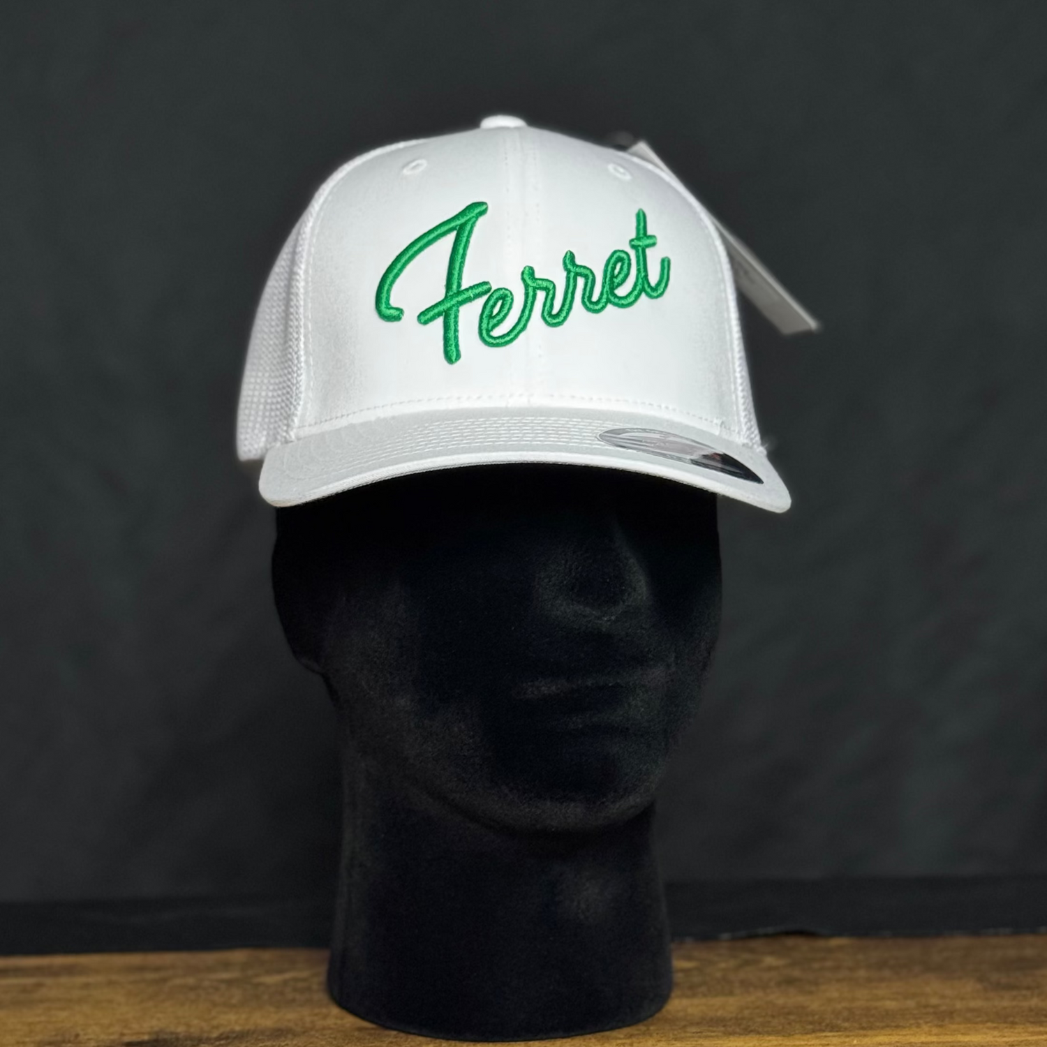 White cap with green Ferret text on a black mannequin head against a dark background