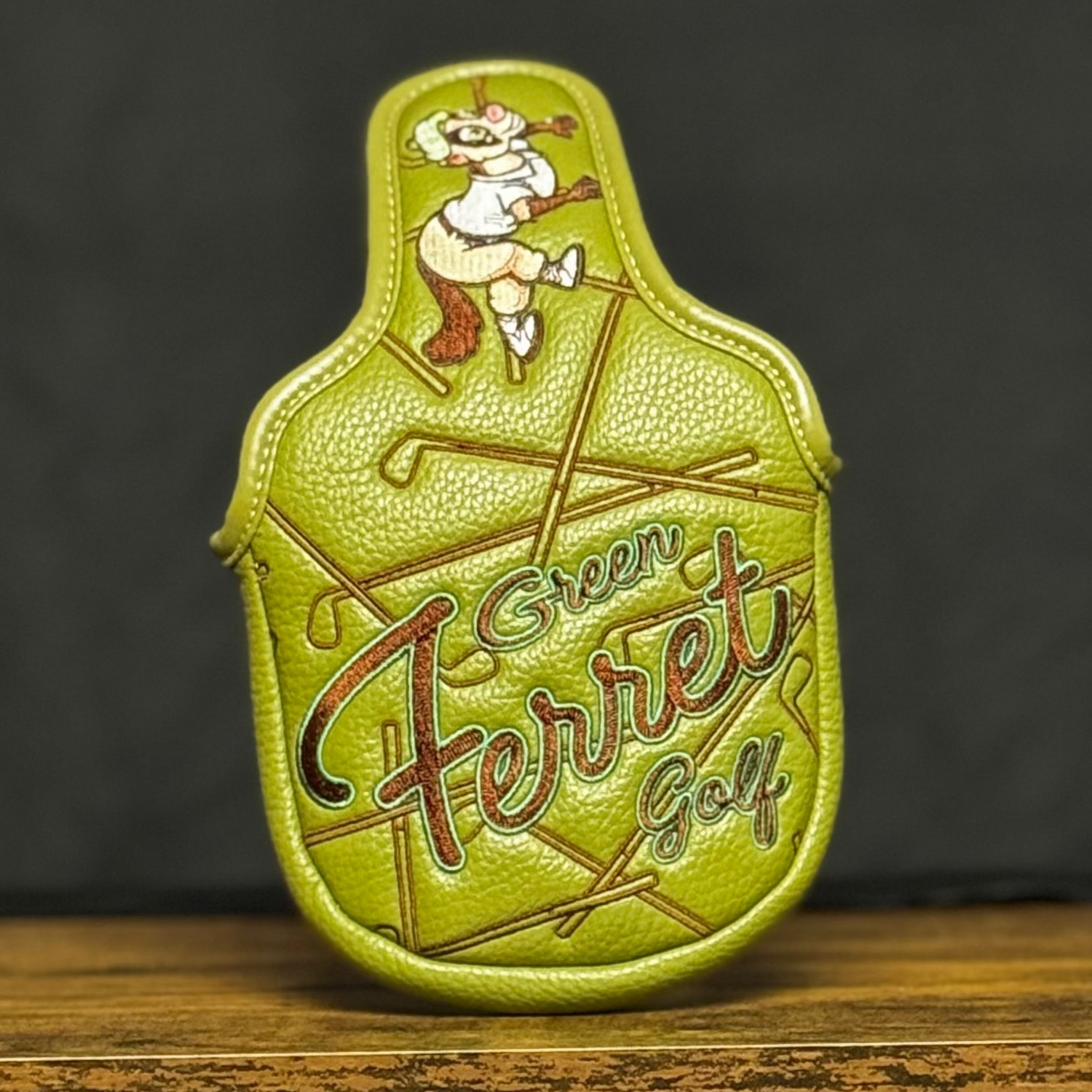 Green Mallet Putter cover with 'Green Ferret Golf' branding on a wooden shelf against a dark textured background.