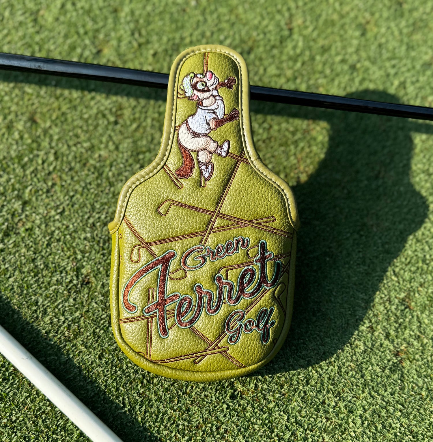 Putter head cover with 'Green Ferret Golf' branding on a green surface
