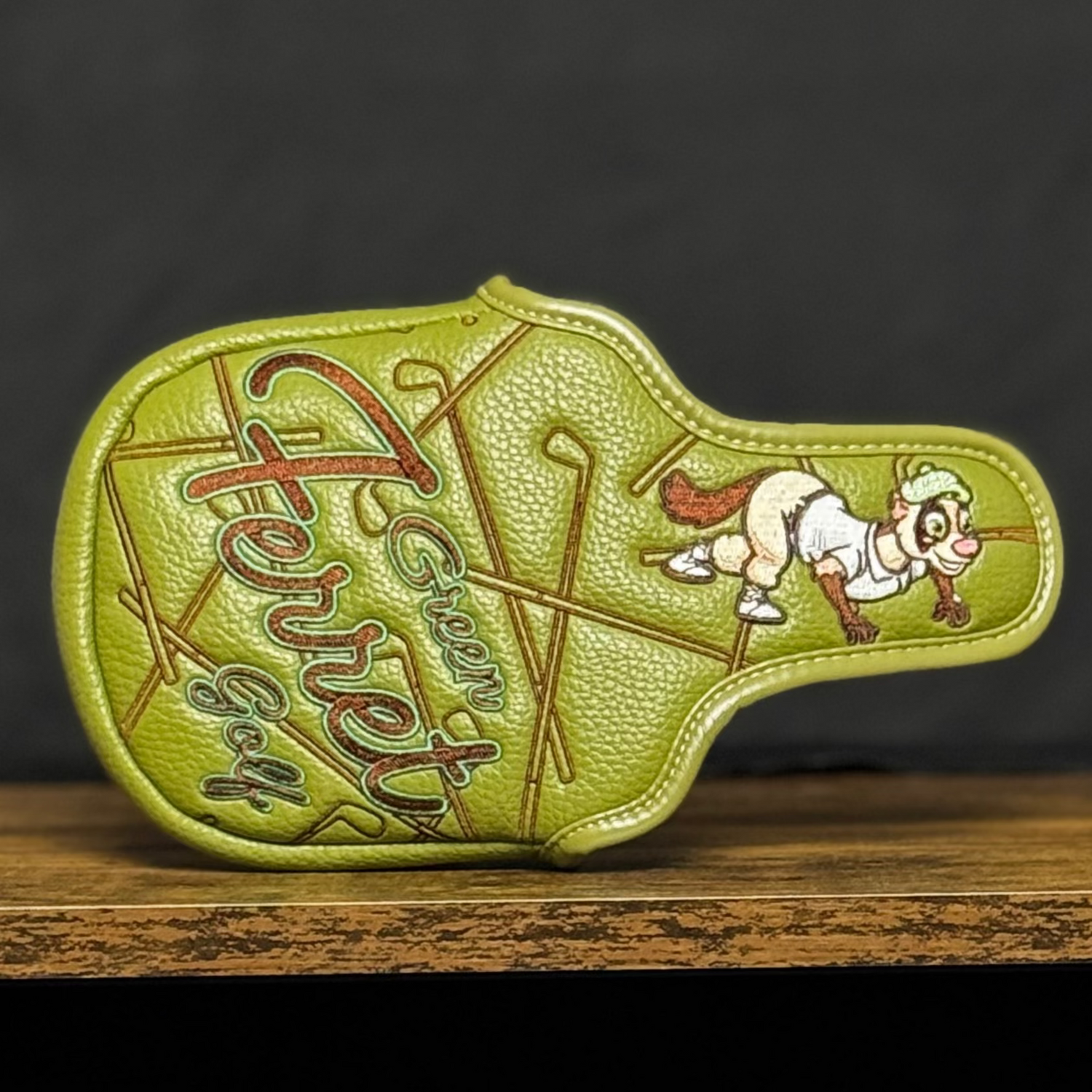Green Mallet Putter cover with 'Green Ferret Golf' branding on a shelf against a black backdrop