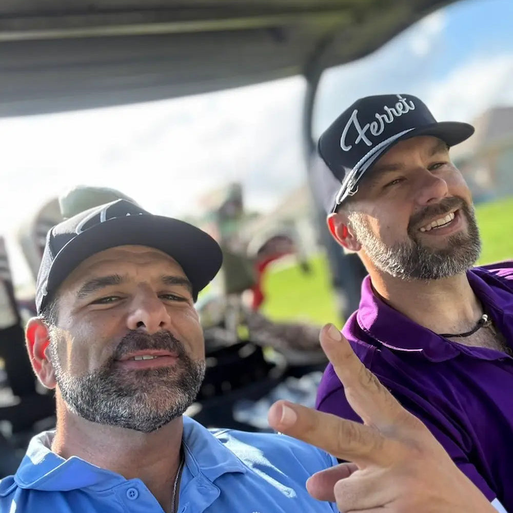 Two men in golf attire sitting in a golf cart on a golf course wearing Green Ferret Golf Essential items.