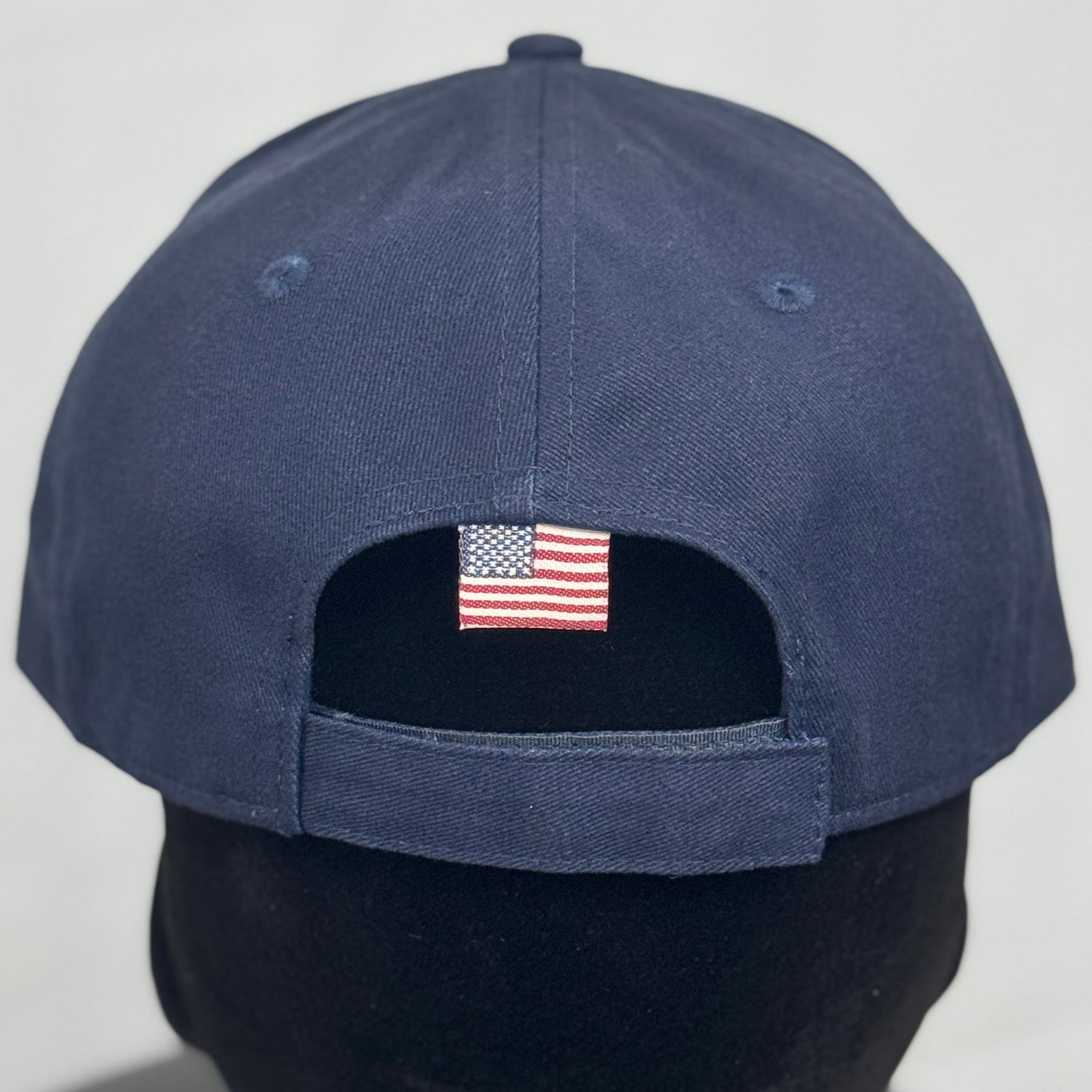 Navy blue baseball cap with American flag patch on mannequin head.